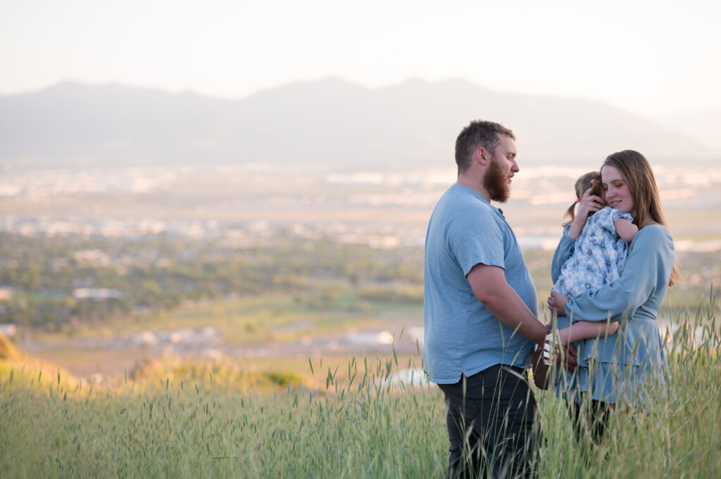Family of three cuddling on the mountainside at sunset for a Utah County Family Photographer.
